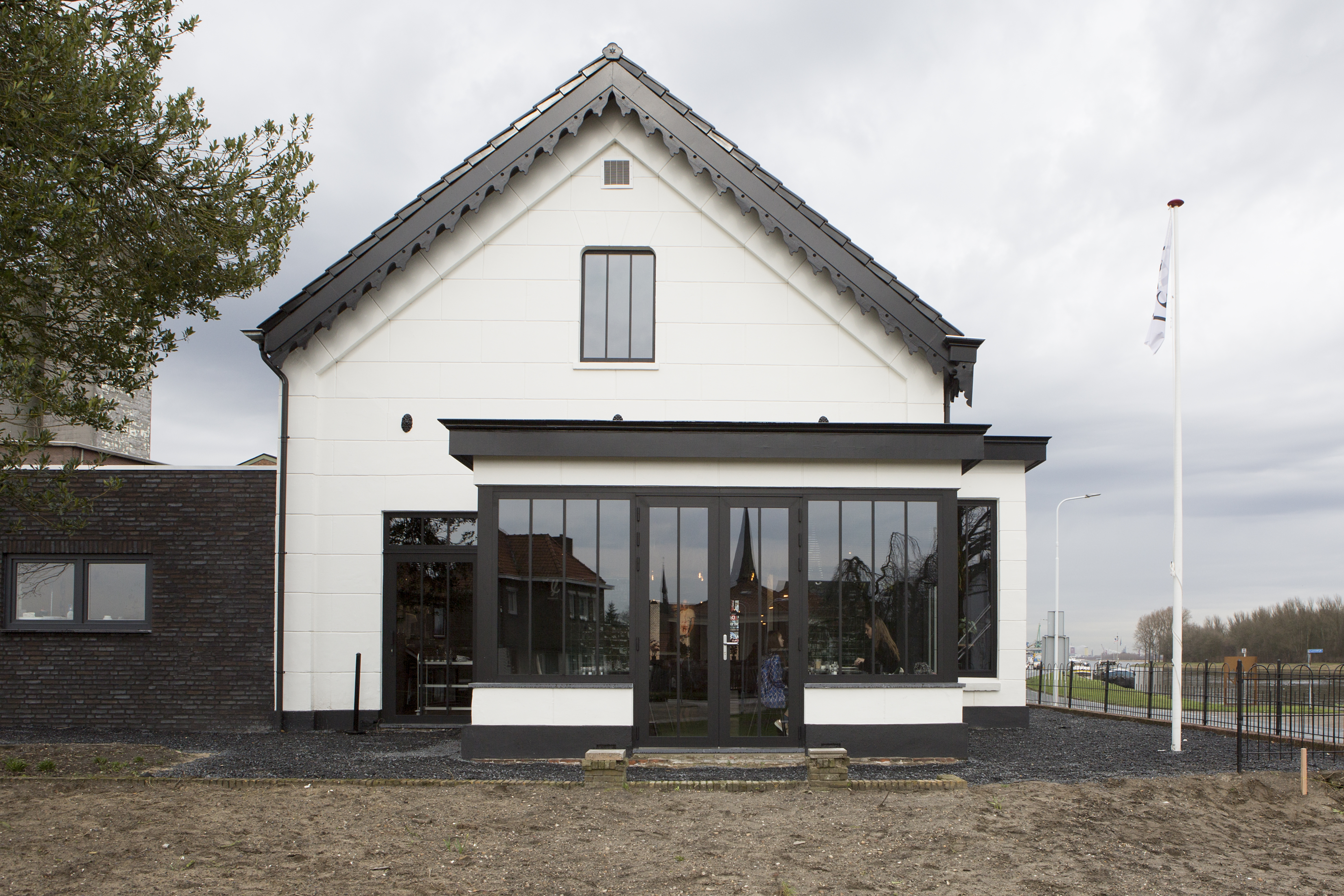 Het huis heeft een modern ontwerp met grote zwartomrande kozijnen en een centrale glazen deur. De kozijnen zijn symmetrisch geplaatst, wat de esthetische aantrekkingskracht vergroot. Het bovenkozijn is kleiner, wat een gebalanceerde uitstraling geeft. De glazen deur dient als hoofdingang en laat natuurlijk licht binnenstromen.