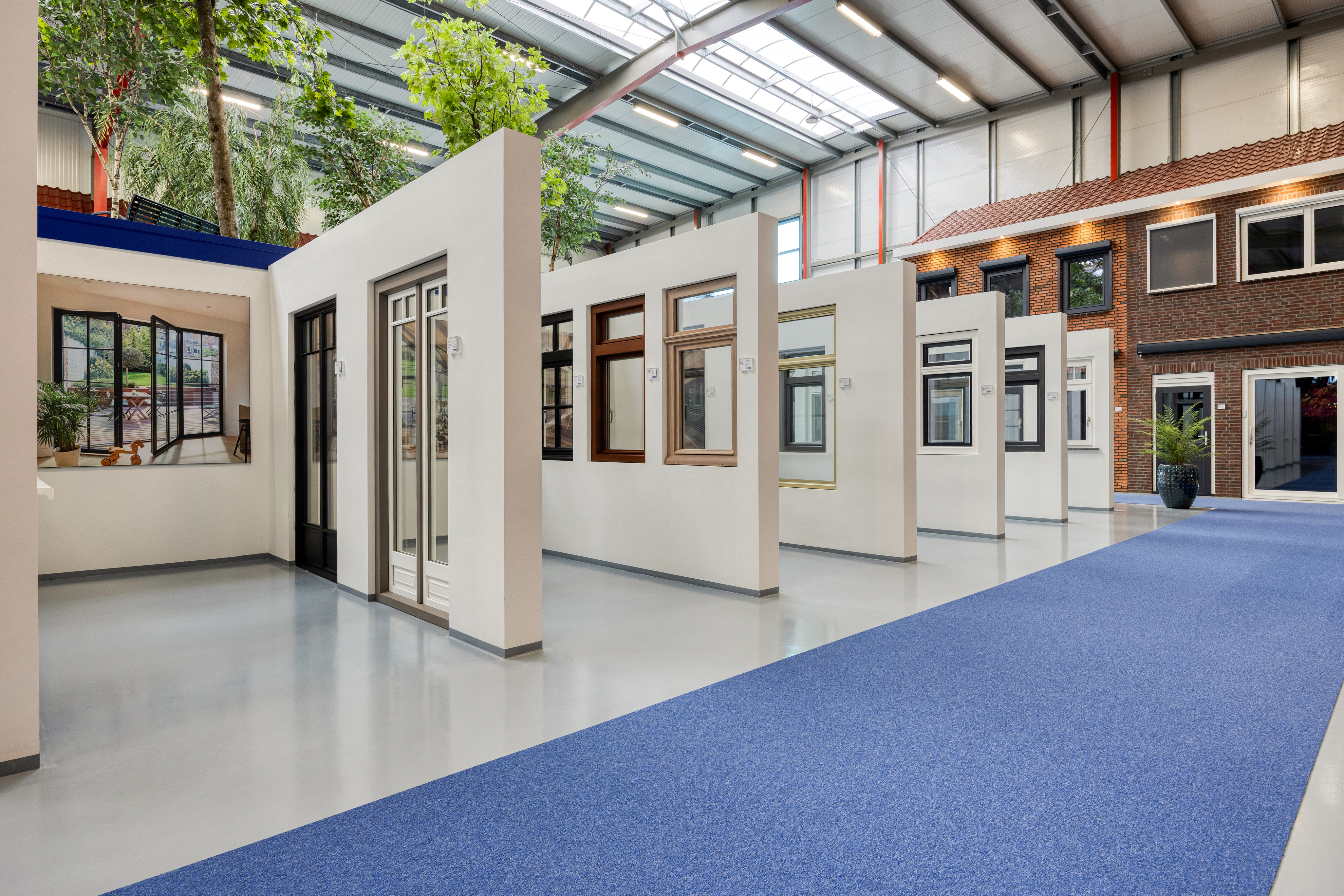 De afbeelding toont een showroom met diverse kozijn- en deurmodellen in een ruime, goed verlichte ruimte. Elke sectie heeft verschillende stijlen en materialen, waaronder houten en metalen kozijnen. De opstelling is overzichtelijk, zodat klanten de opties gemakkelijk kunnen bekijken en vergelijken.