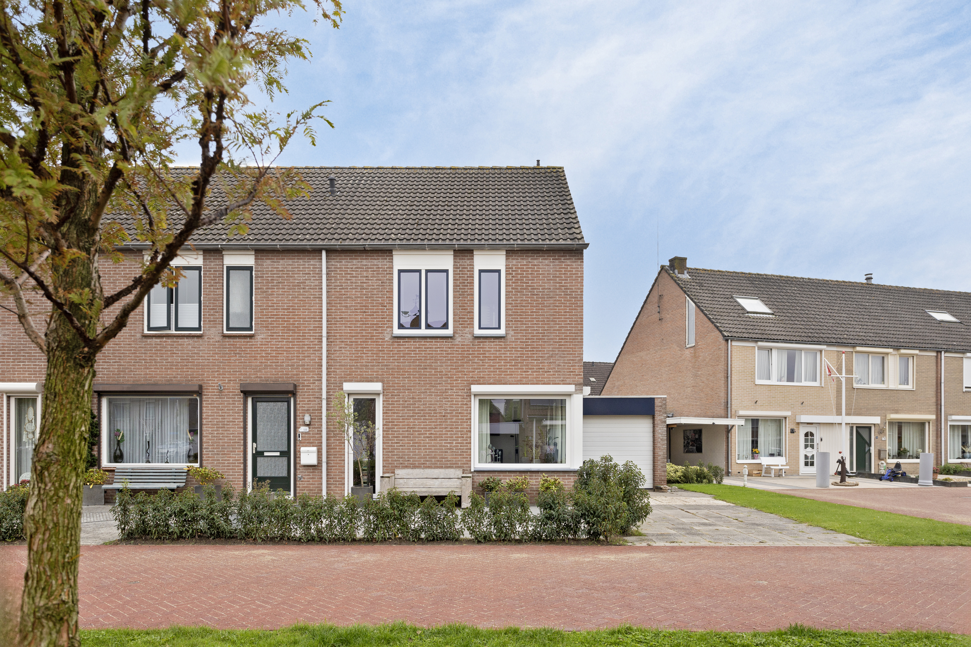 De afbeelding toont een rij moderne bakstenen huizen met grote kozijnen en deuren. De kozijnen zijn rechthoekig en symmetrisch geplaatst, wat een evenwichtige uitstraling geeft. De deuren zijn eenvoudig en passen bij het algehele ontwerp van de huizen. De voortuinen zijn netjes onderhouden, wat bijdraagt aan de esthetische aantrekkingskracht.