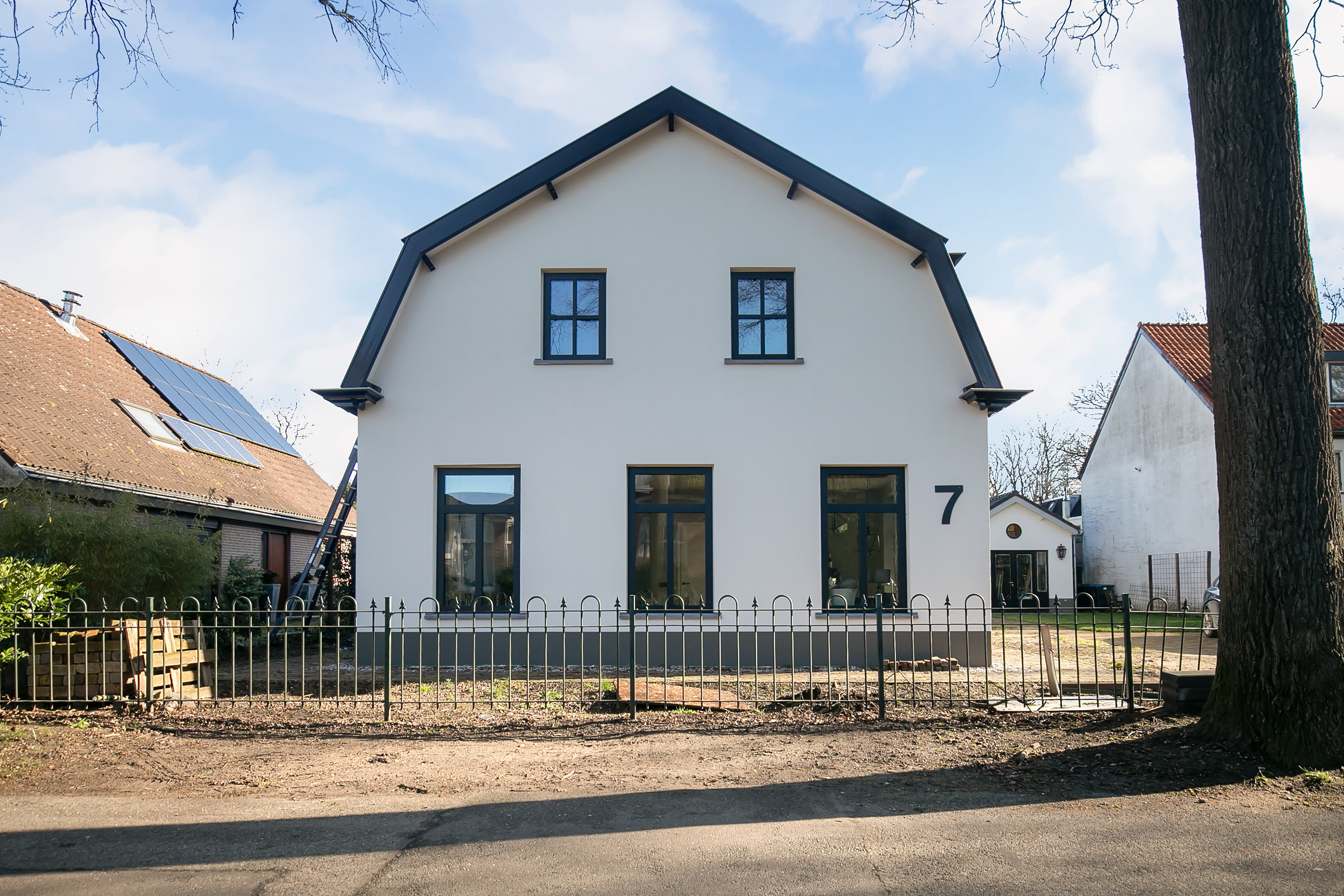 Het huis heeft een modern ontwerp met een symmetrische gevel. Er zijn vier grote kozijnen op de begane grond en twee kleinere boven. De kozijnen zijn omlijst met donker materiaal, wat contrasteert met de witte muren. Een centrale deur ontbreekt, waardoor de kozijnen opvallen.