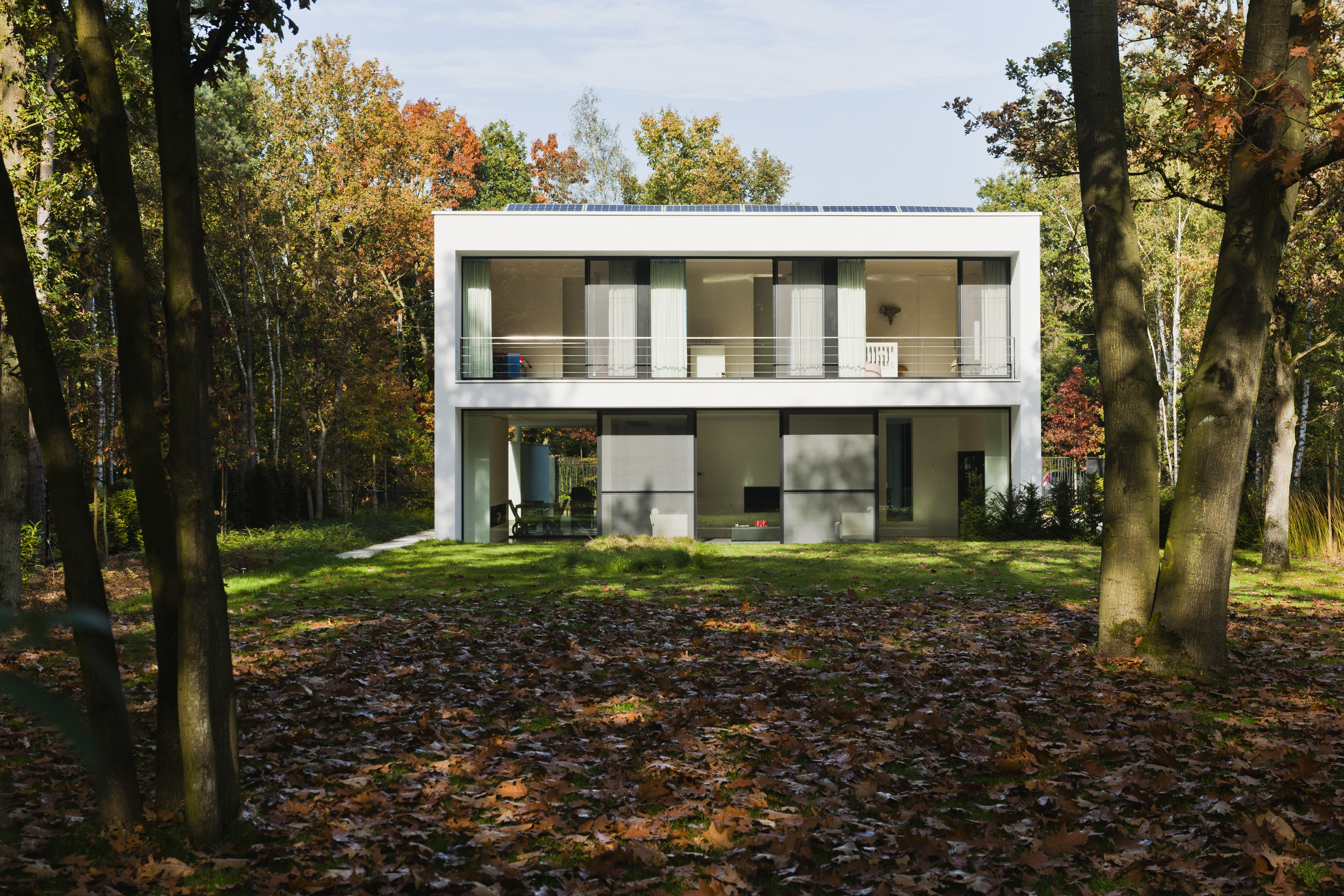 Het moderne huis heeft grote schuiframen en deuren, die een naadloze verbinding tussen binnen en buiten bieden. De bovenverdieping heeft uitgestrekte glaspartijen, waardoor natuurlijk licht het interieur overspoelt. Het minimalistische ontwerp legt de nadruk op strakke lijnen en functionaliteit.