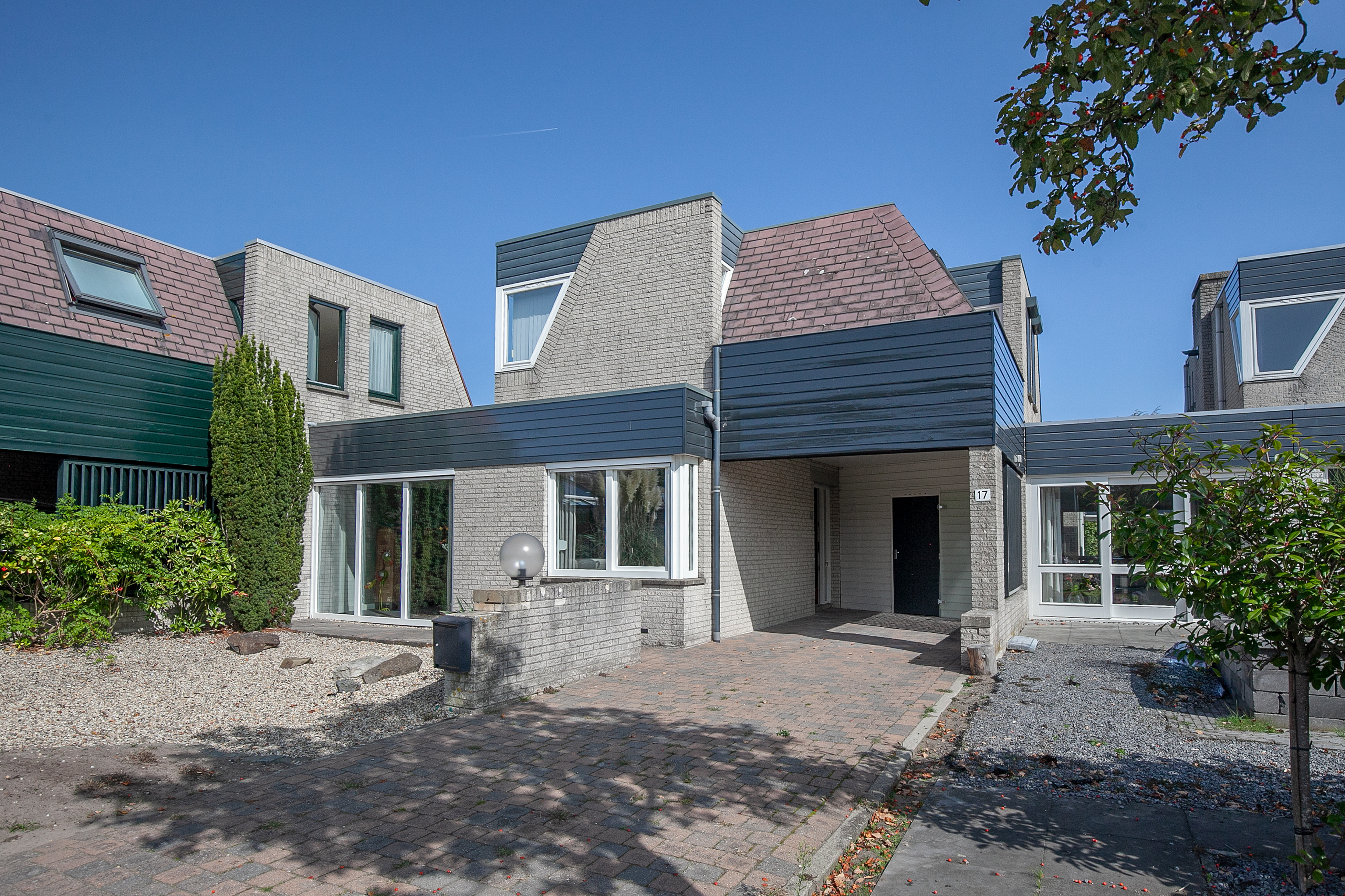 Het huis heeft grote schuifpuien en een moderne voordeur. De kozijnen laten veel natuurlijk licht binnen, wat het moderne ontwerp van de woning versterkt. De voordeur is strak en past bij de algemene esthetiek.