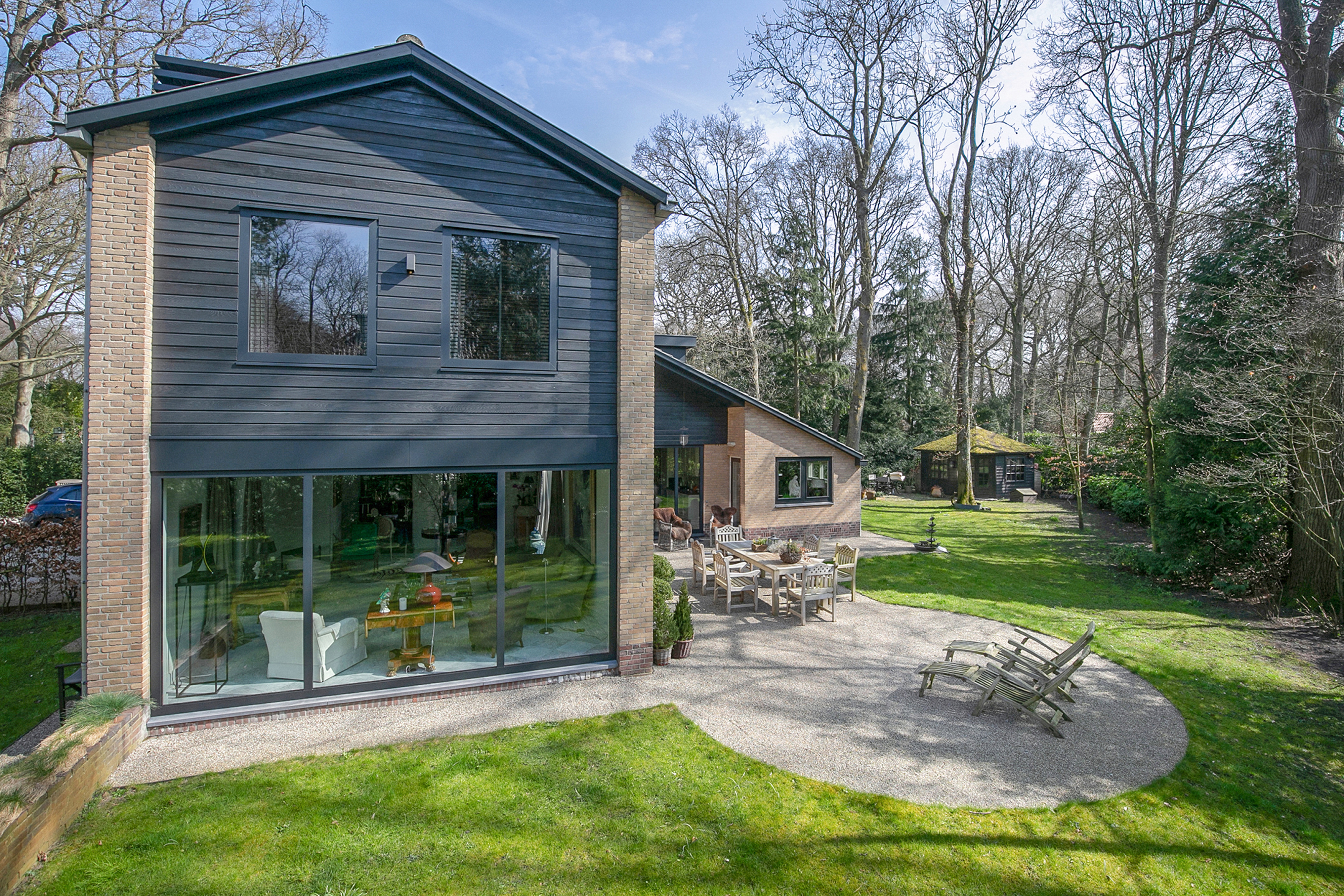 Het huis heeft grote schuifpuien op de begane grond, die een naadloos uitzicht op de tuin bieden. Op de bovenverdieping zijn er twee standaardkozijnen die natuurlijk licht binnenlaten. De deuren zijn modern en passen bij het strakke ontwerp van het huis.